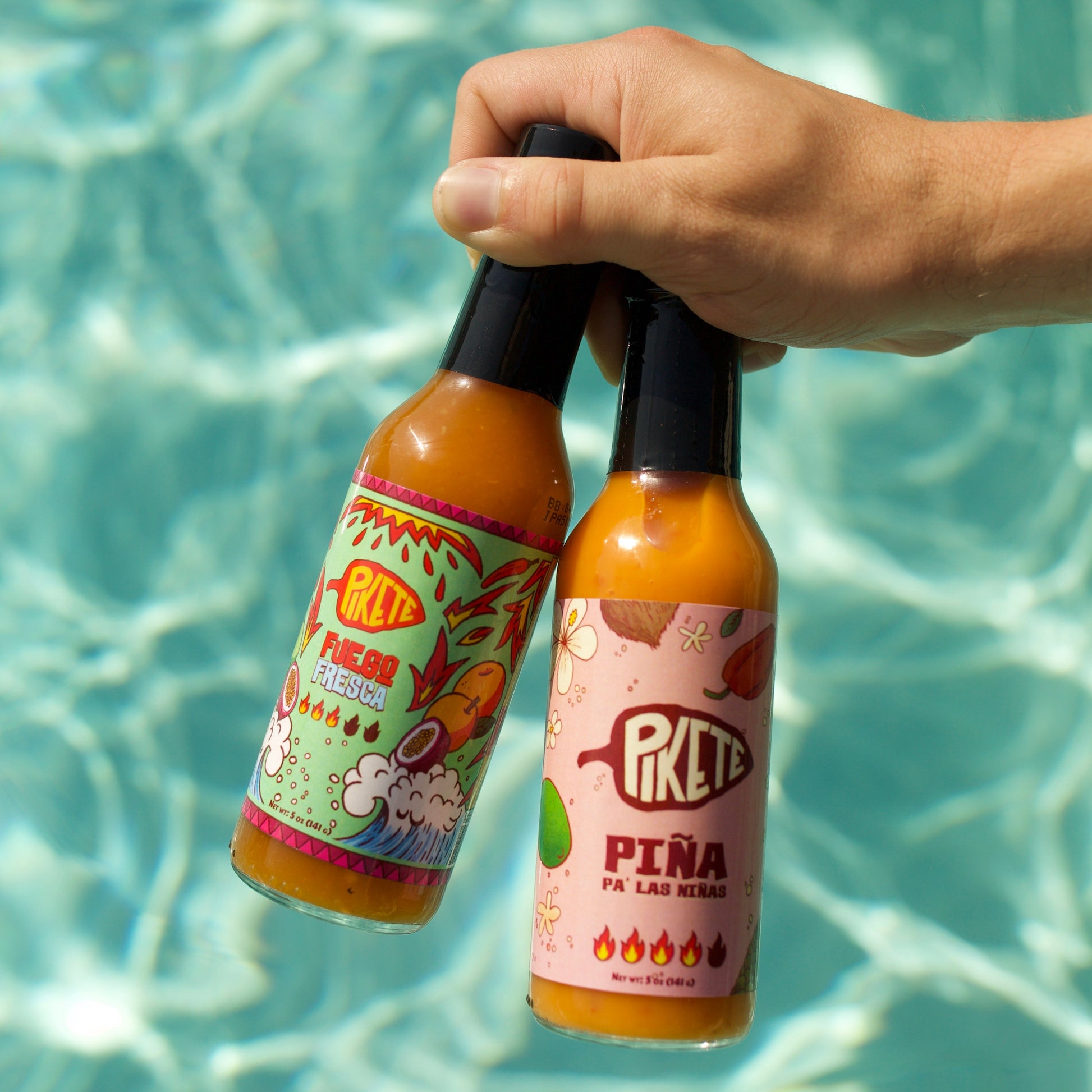 Two bottles of hot sauce held above a pool with water below