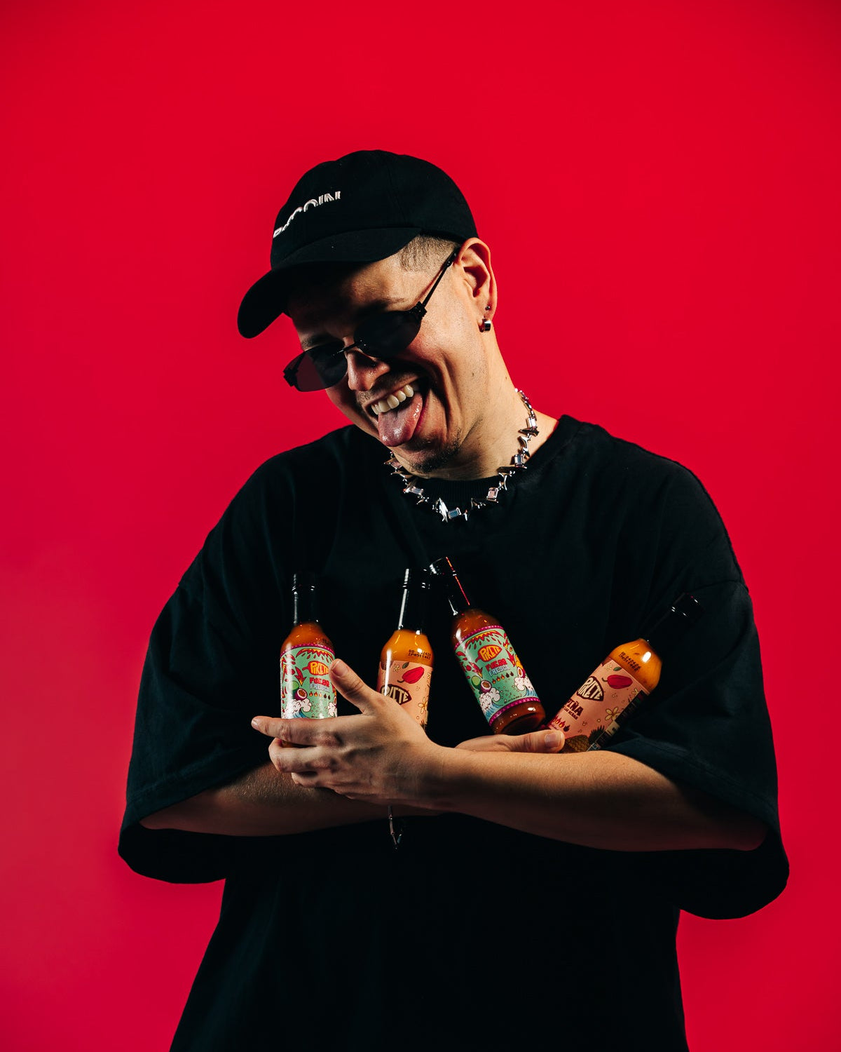 Person holding hot sauce bottles against a red background