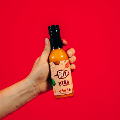 Hand holding a bottle of hot sauce against a red background
