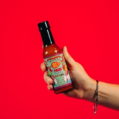 Hand holding a hot sauce bottle with colorful label against a red background