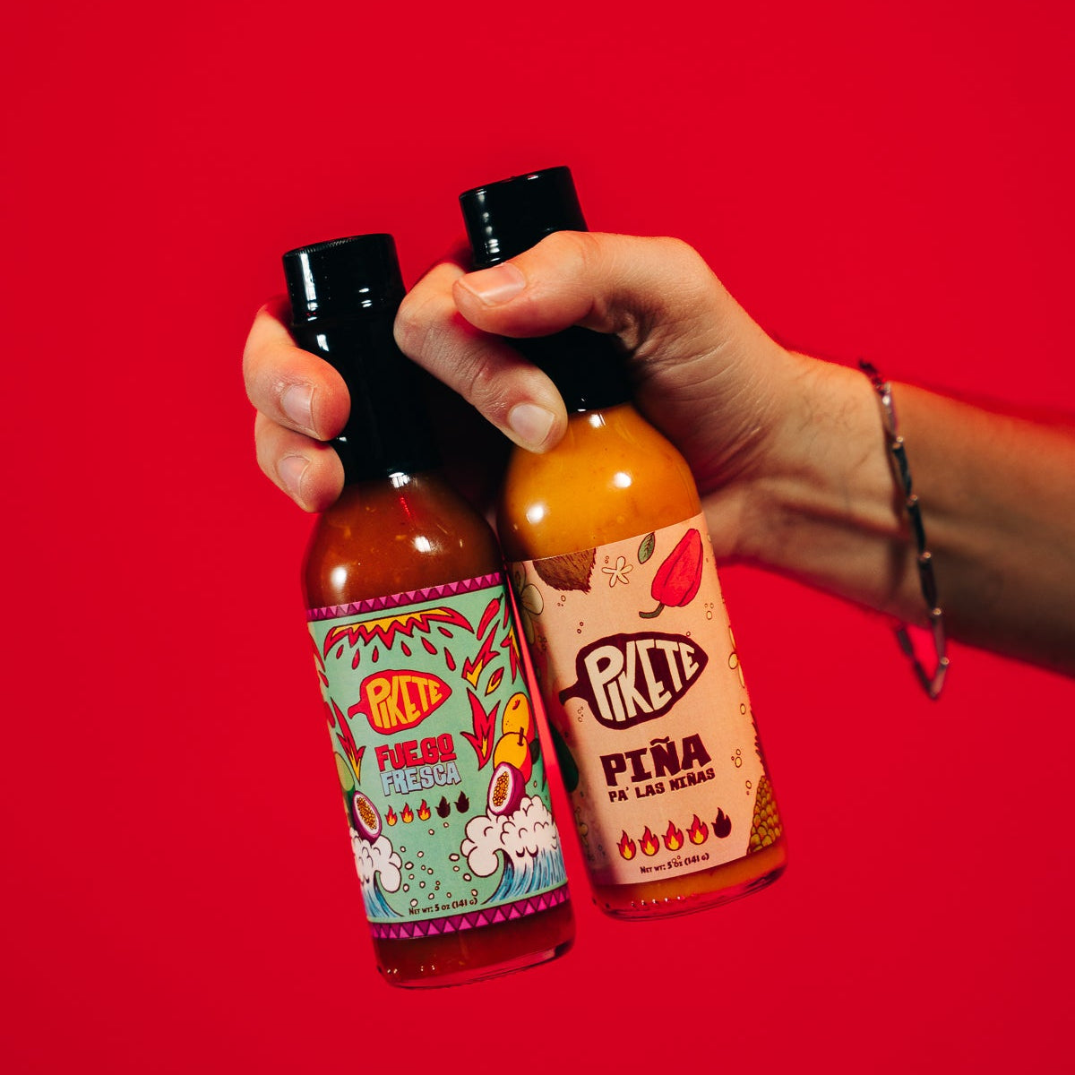 Two bottles of hot sauce held against a red background